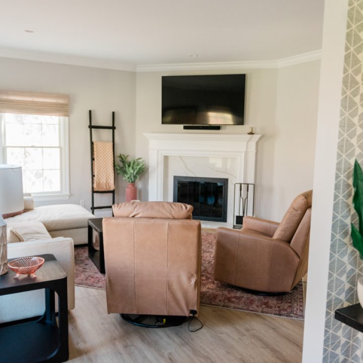 A warm, welcoming living room featuring a white marble fireplace, wall-mounted TV, leather recliner, beige sofa, and layered rugs — designed for comfort, style, and seamless daily living in this remodeled home.